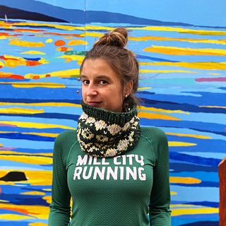 Woman in front of a colorful mural wearing a hand knit cowl
