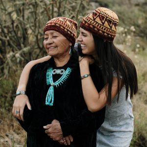 A photo of two Navajo women, one younger and one older. They both wear hand knit hats.