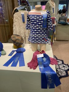 Photo of knit gloves, sweaters, and hats with Minnesota State Fair ribbons and rosettes. 