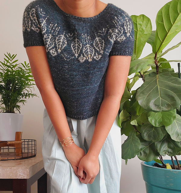 The torso of a woman in a hand knit grey sweater with cream color work