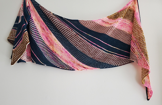 A hand knit shawl with diagonal stripes in pinks and black