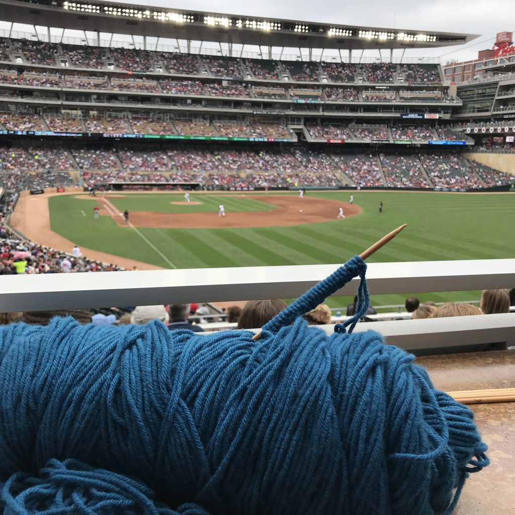 A skein of blue yarn with a needle stuck in it with Target Field baseball field in the background