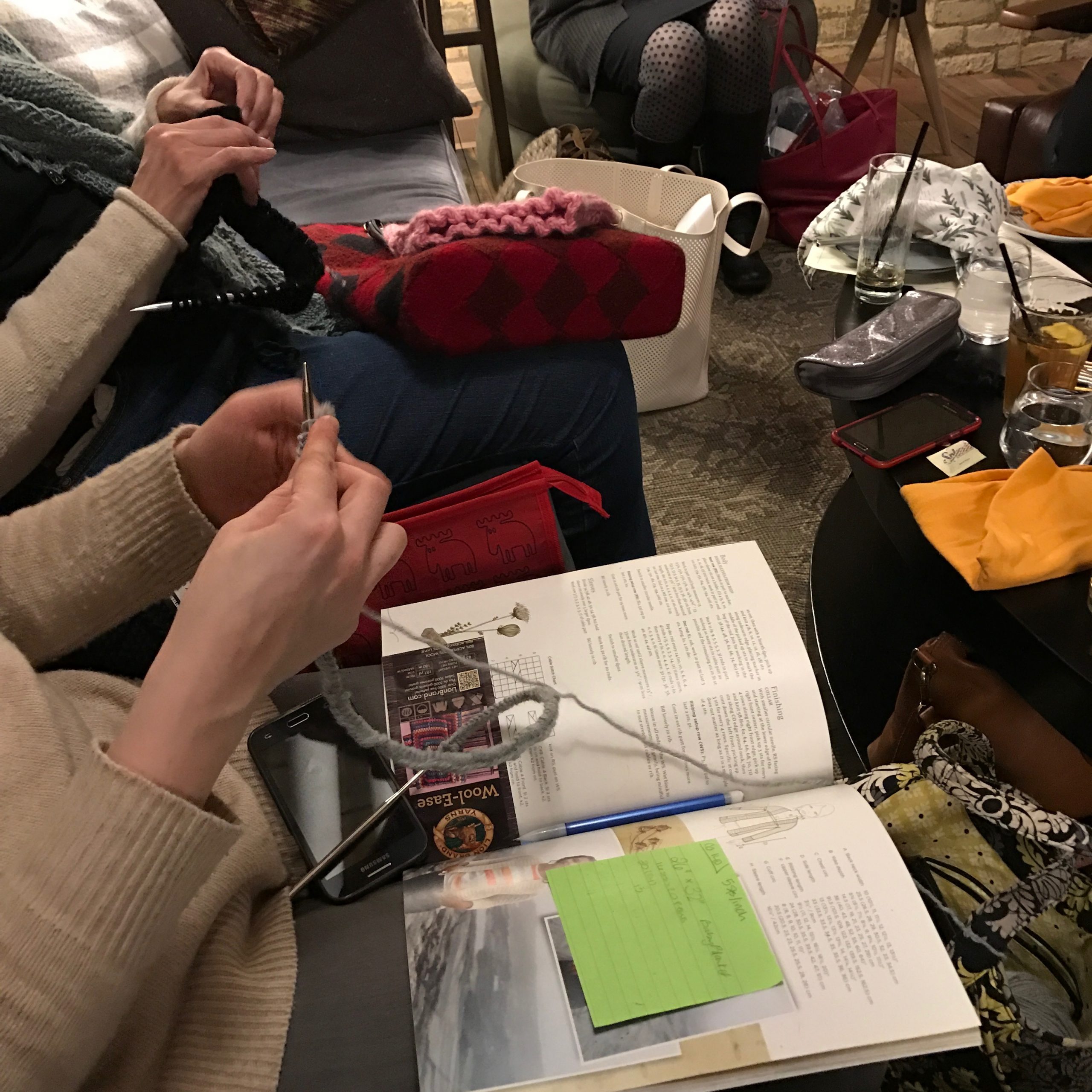 A group of woman knitting, the image only shows their laps and hands.