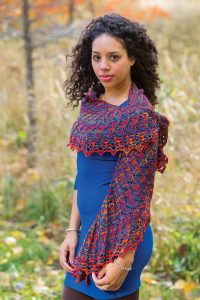 A black woman in a blue dress wears a knit lace shawl in multiple colors.