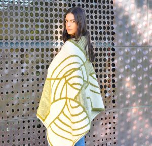 Woman wearing a hand knit, gold and white cape.