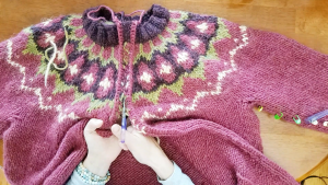 A pink sweater with a colorwork yoke being cut open for a steek.