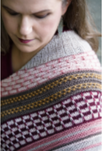 A woman wearing a multi-colored, multi-patterned, hand knit shawl.