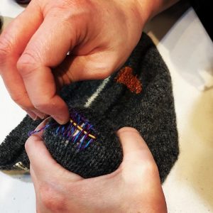 Close up of hands darning a hole in knitting