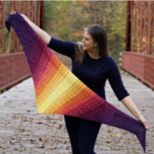 Woman holding up a triangular shawl knit in multi-color stripes.