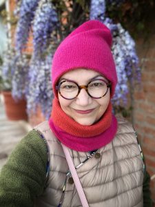 Woman in round glasses wearing a pink hat and cowl.