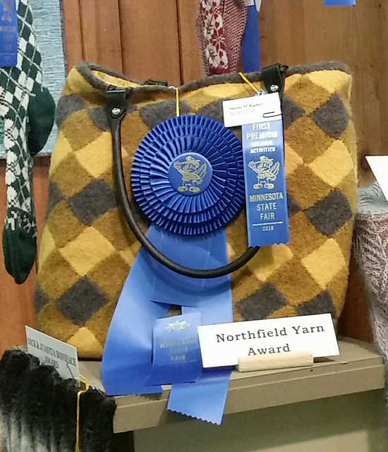 A knit and felted plaid purse in yellow, brown, and black. It has state fair prize ribbons on it.