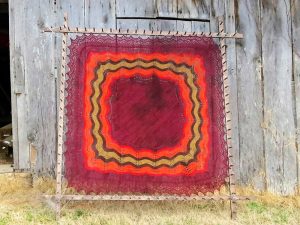 A red and orange hap shawl blocking on a wooden frame.