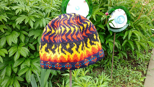A knit hat with orange and red flame design on a background of green leaves