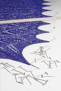 A blue shawl with t-pins and a ruler on white.