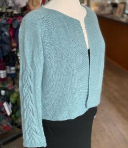 light blue cardigan with a cable design down the bottom half of the sleeve