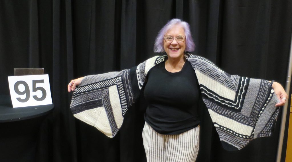 Woman modeling a black, white & grey hand knit shawl