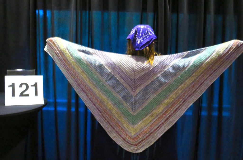Woman modeling a hand knit shawl in muted rainbow colors