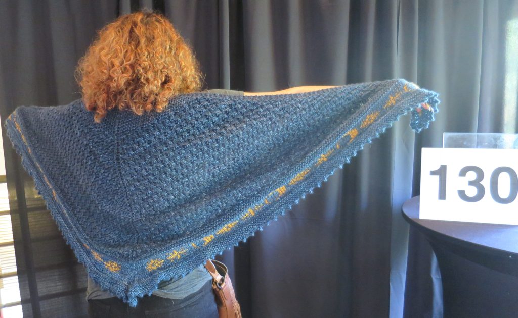 A woman models a hand knit blue shawl