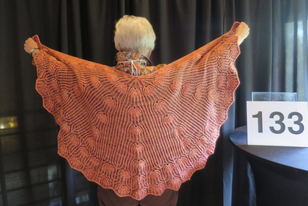 A woman models a coral hand knit shawl