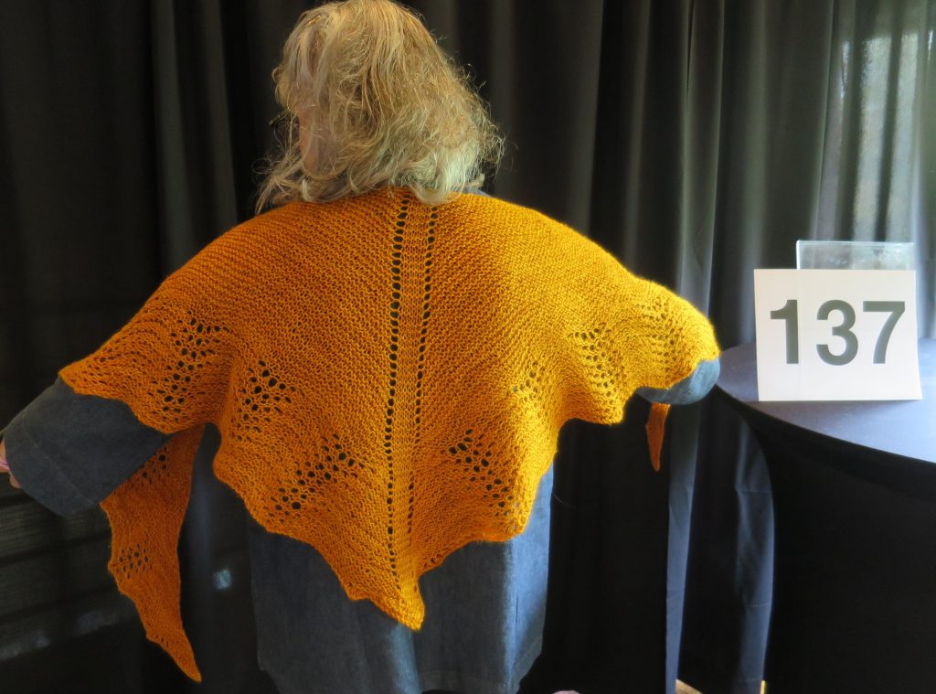 A woman models a hand knit orange shawl