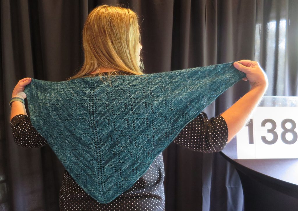 A woman models a hand knit blue shawl