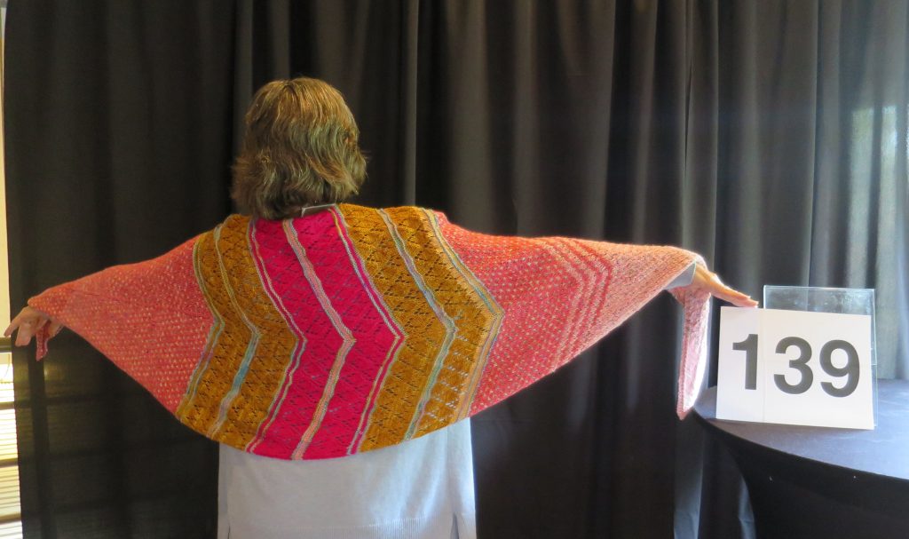 A woman models a pink & gold hand knit shawl