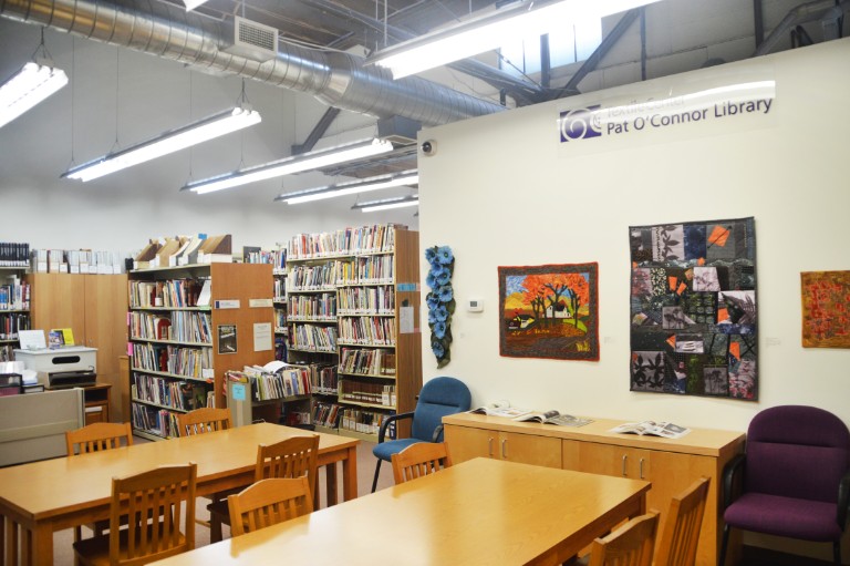 photo of the Textile Center Library with wooden tables and chairs and shelves of books.