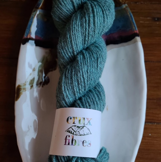 A skein of blue yarn labled Crux Fibres on a plate