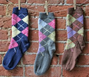 photo of three argyle socks hanging from clothespins against a red brick wall.