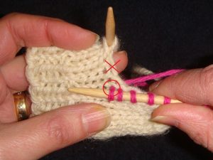 Hands knitting on double pointed needles with pink yarn on white yarn