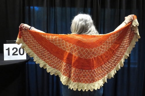 Woman with grey hair seen from the back showing off a hand knit yellow & orange shawl.