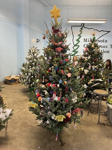 A christmas tree with hand knit decorations and pompom garland.