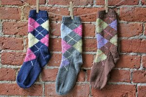 Three argyle socks hang from clothes pins against a brink wall