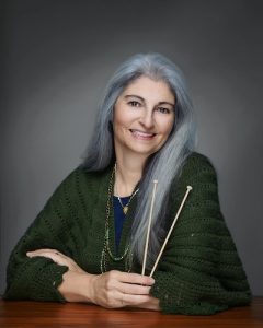 Photo of a woman with long grey hair holding knitting needles.